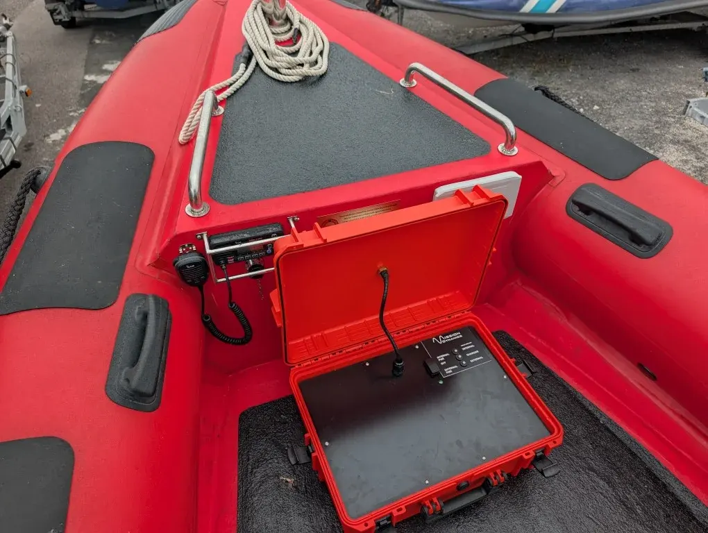 BRNKL Portable case open in a RIB bow locker, showing the Mission Dynamics status panel and connected antenna lead
